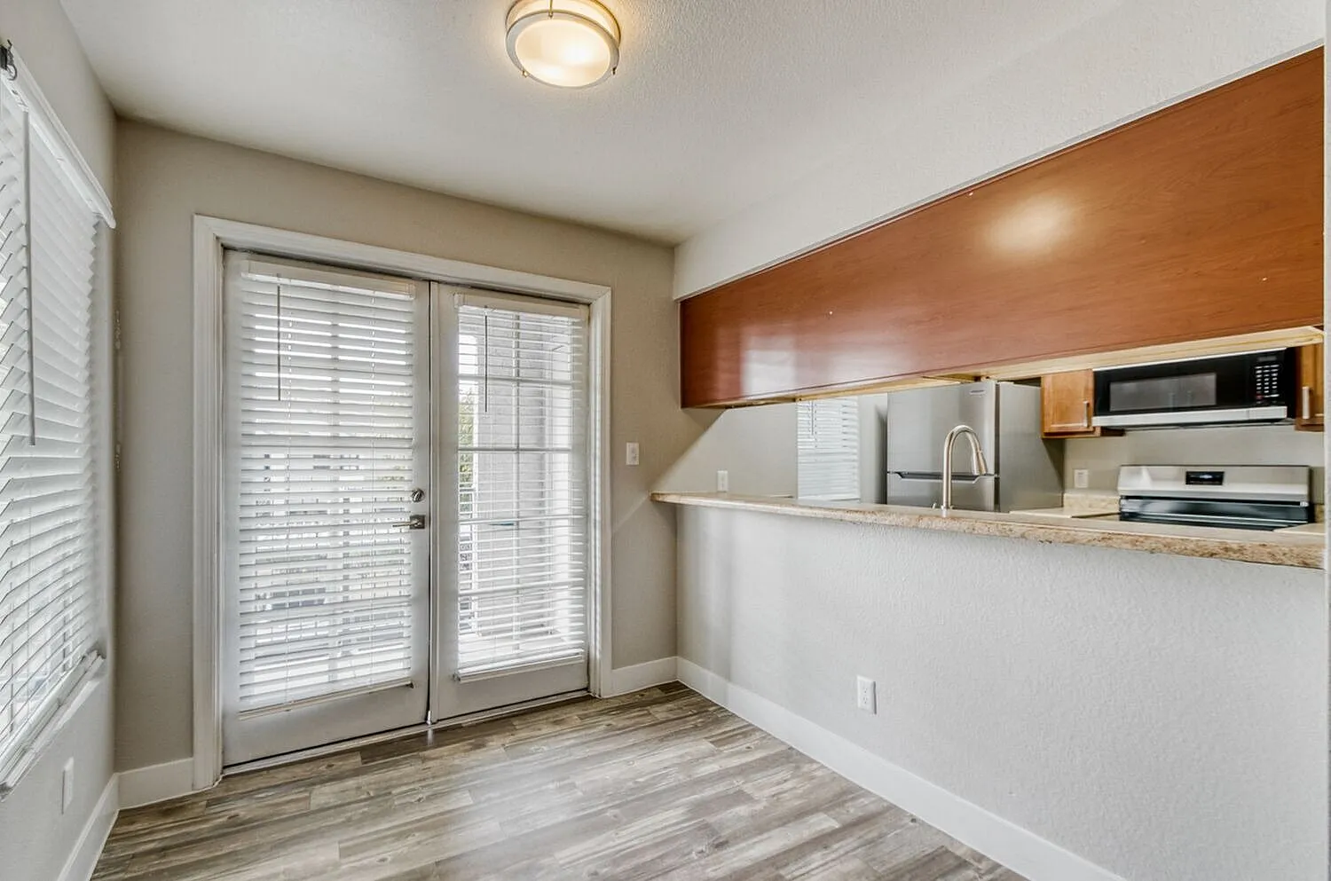 Kitchen with wood-style plank flooring, white cabinetry, granite countertops, stainless appliances, glass entry doors