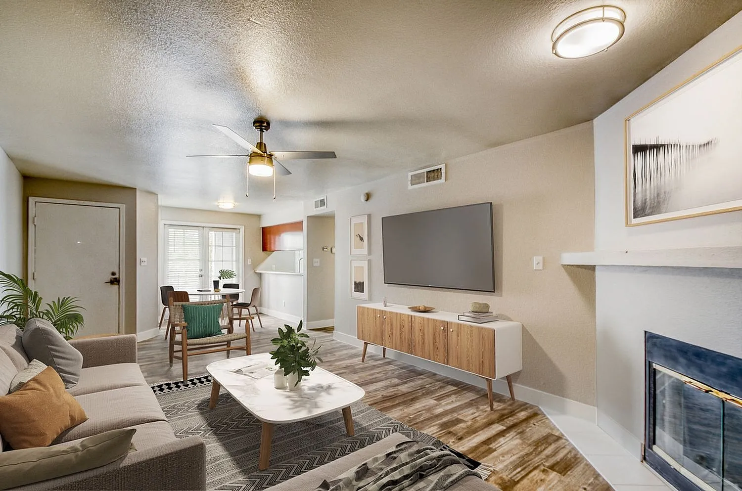 Living room with wood-style plank flooring, ceiling fan, flat-screen TV, fireplace, white cabinetry