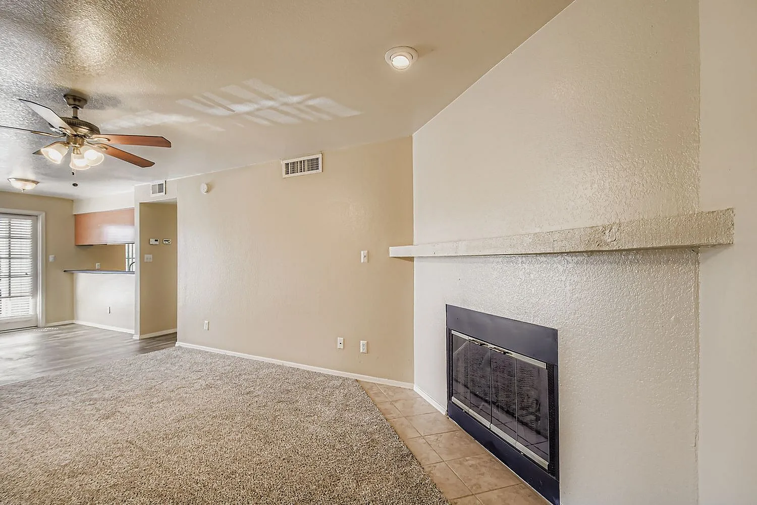 Living room, gas fireplace with stone surround, wood-style plank flooring, ceiling fan, textured walls