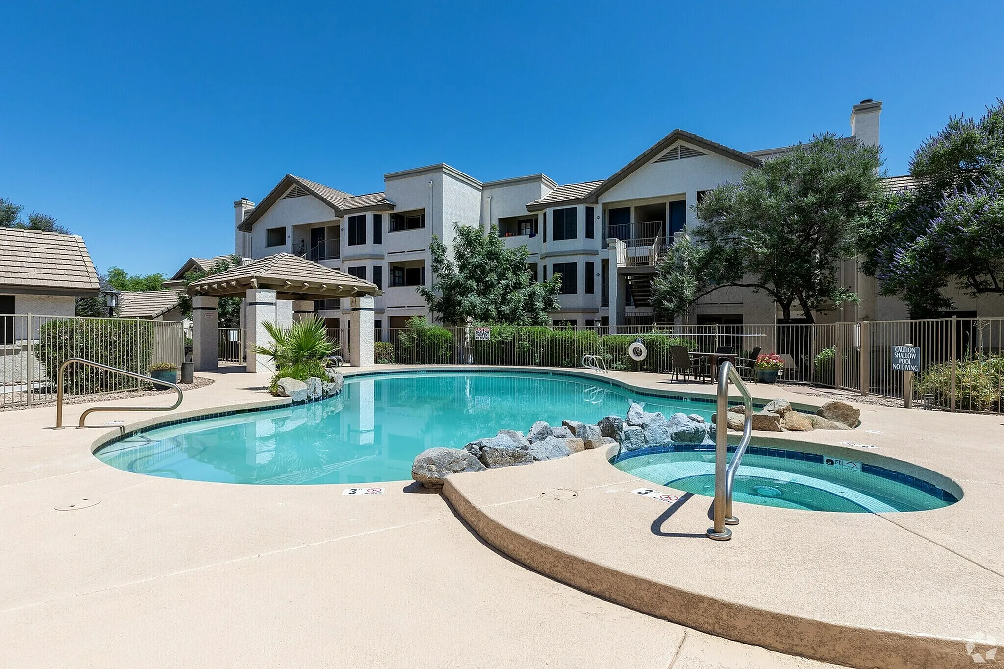 Community pool and spa, lounge area, multi-story residential buildings, clear blue sky