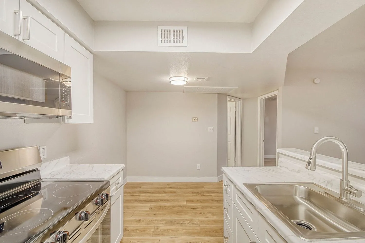 Kitchen, white shaker cabinetry, stainless steel appliances, wood-style plank flooring, quartz countertops