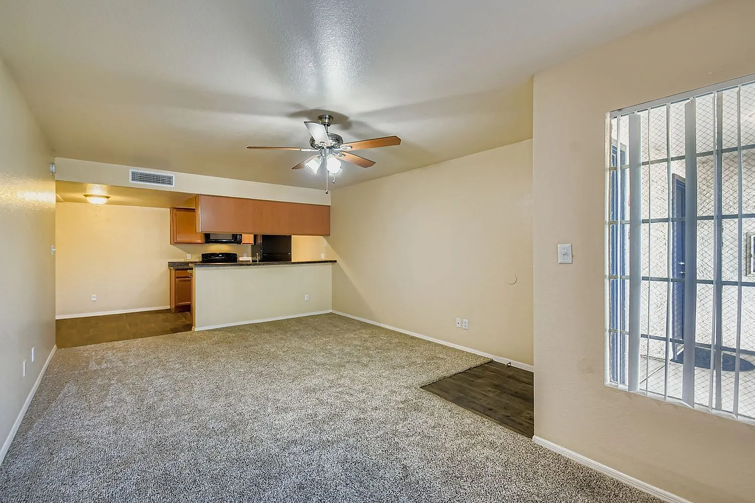 Living room with gray carpet flooring, ceiling fan, open kitchen with wood cabinetry