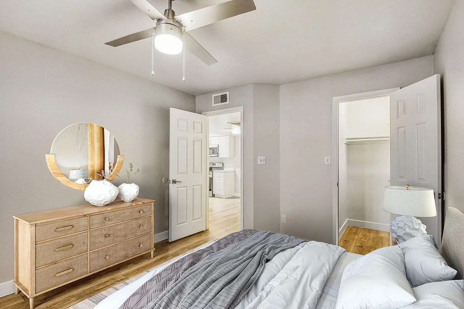 Primary bedroom, wood-style plank flooring, ceiling fan with light, wooden dresser with round mirror