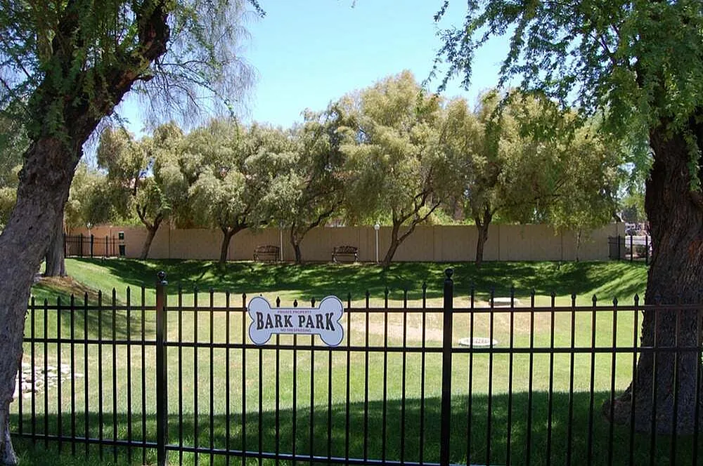 Bark park, black metal fence, manicured grass, mature trees, adobe walls