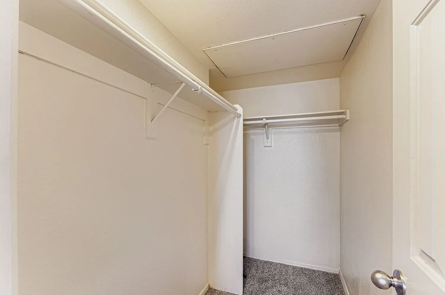 Walk-in closet, metal shelving rods, white walls, carpet flooring