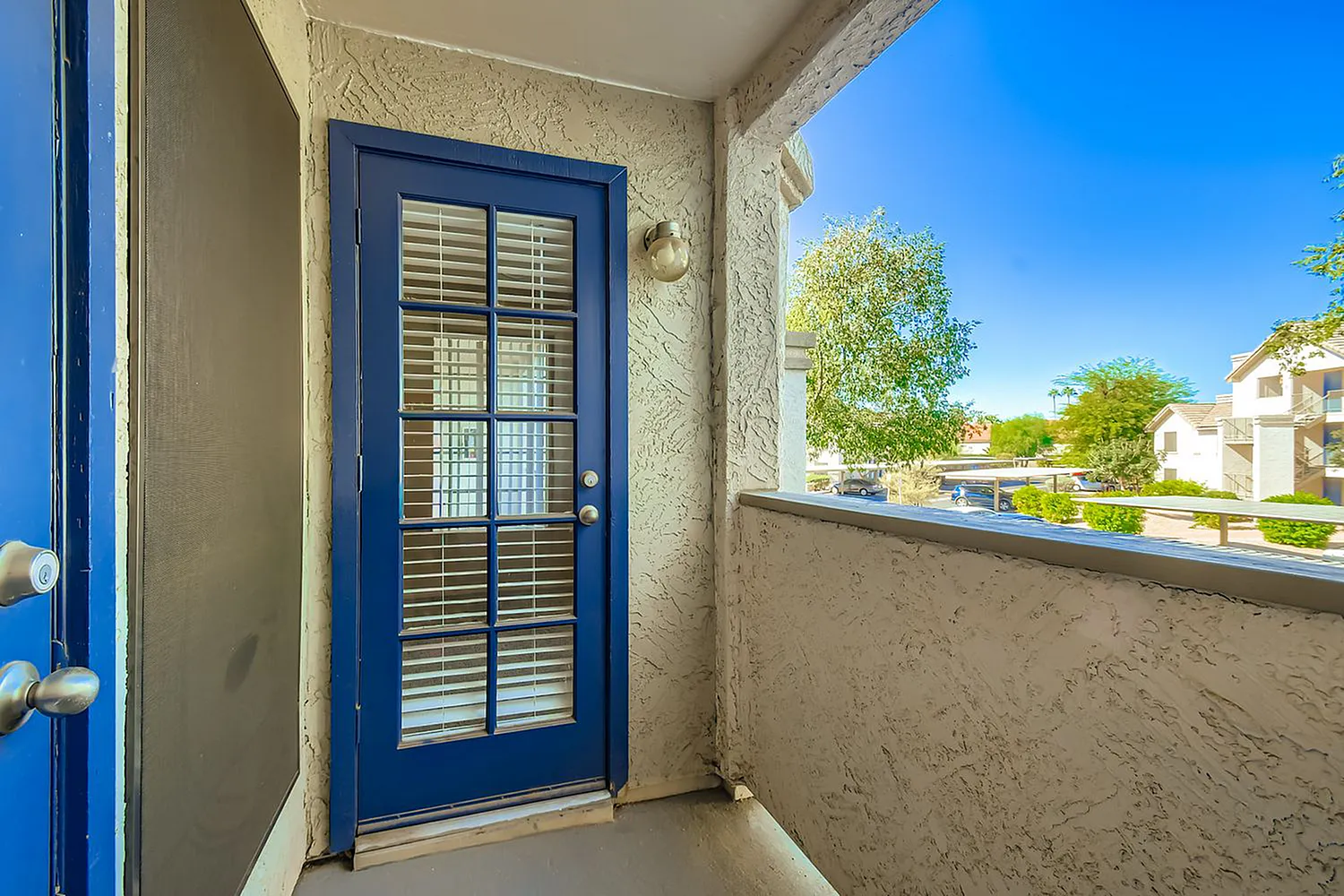 Covered patio area, blue entry door with louvered glass, concrete railing, neighborhood view