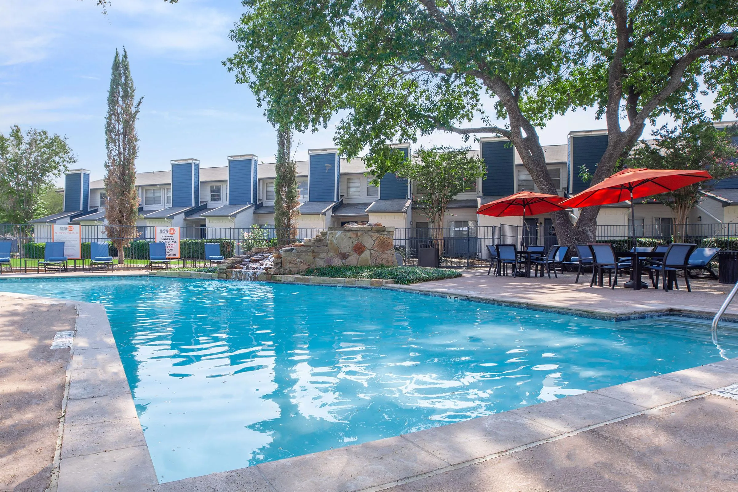 Community pool, stacked stone waterfall, lounge chairs, red umbrellas