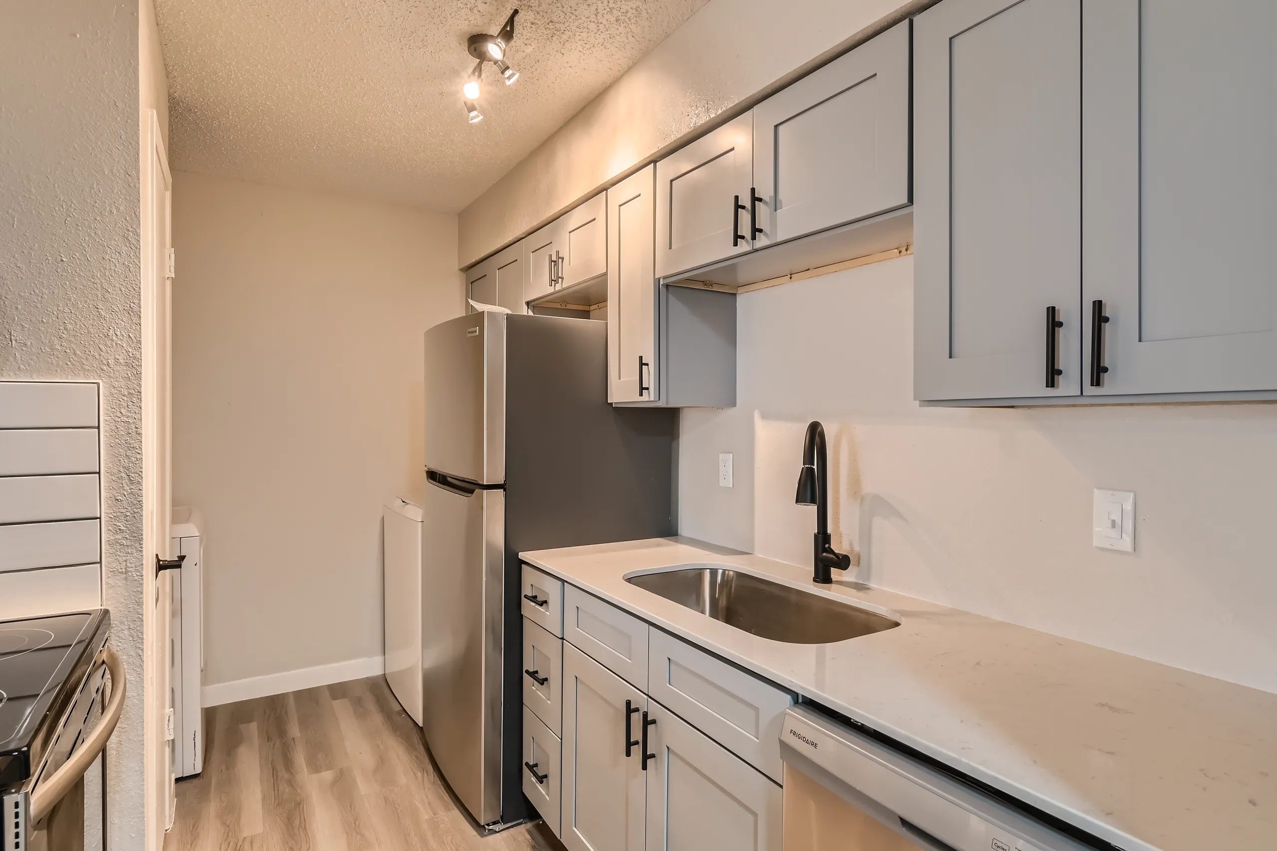 Kitchen with gray cabinetry, stainless refrigerator, and quartz countertops