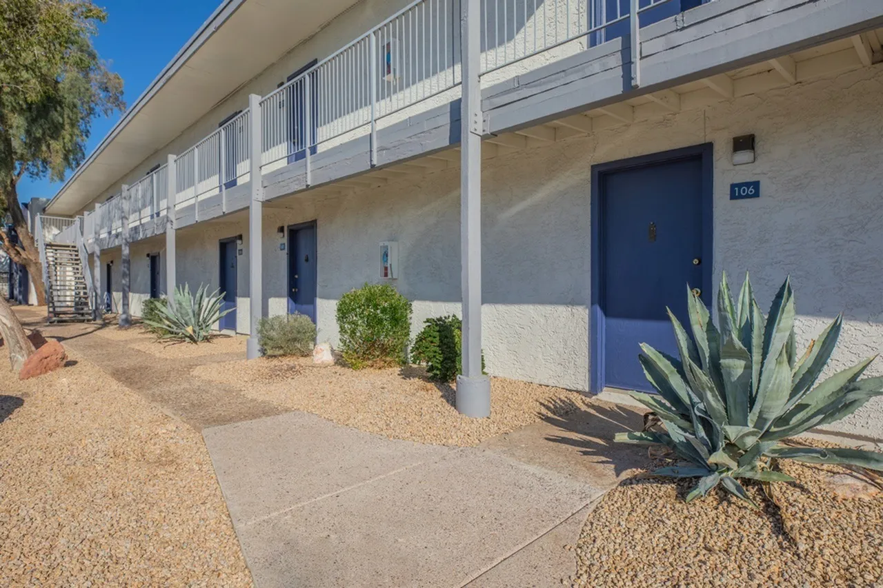 Exterior courtyard, blue entry doors, white metal railings, desert landscaping, gravel pathways
