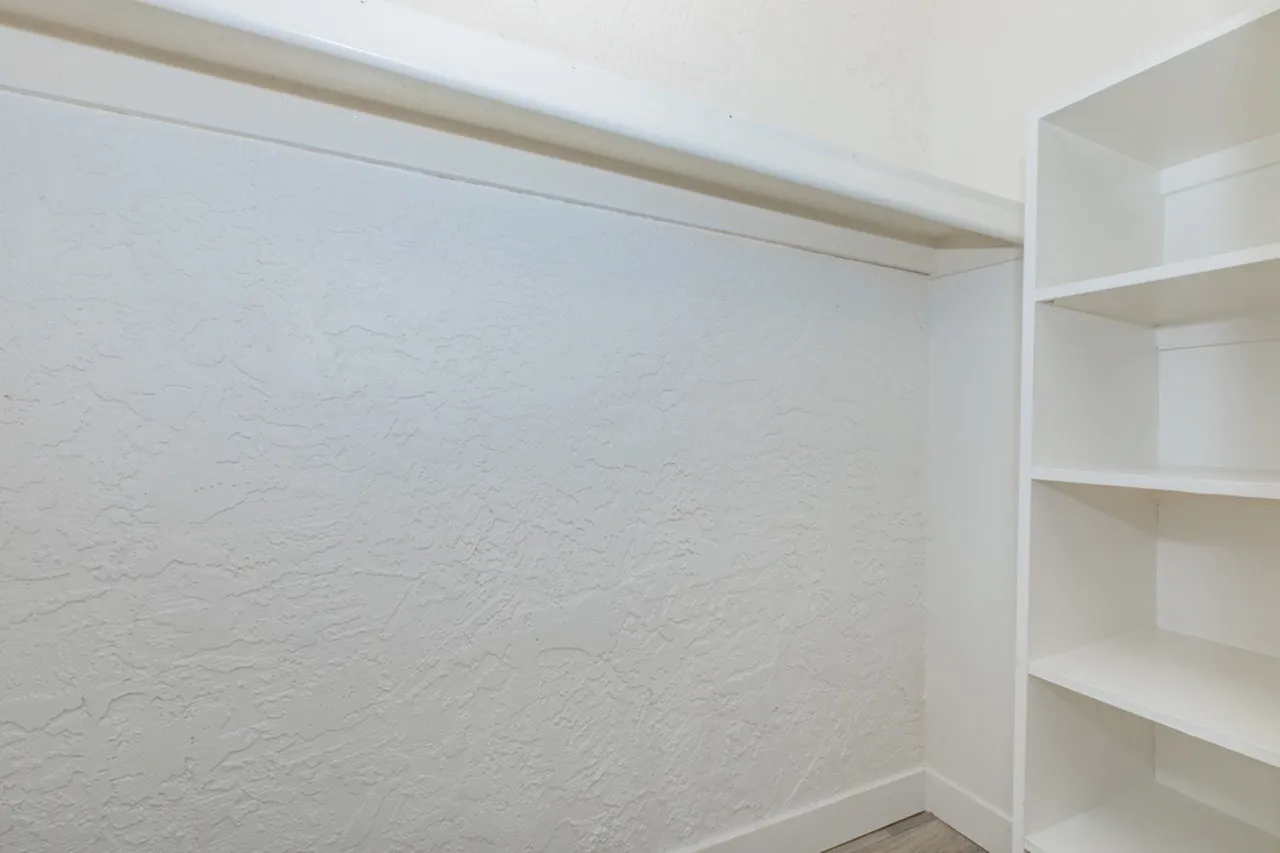 Bedroom closet, white built-in shelving, textured walls, recessed lighting
