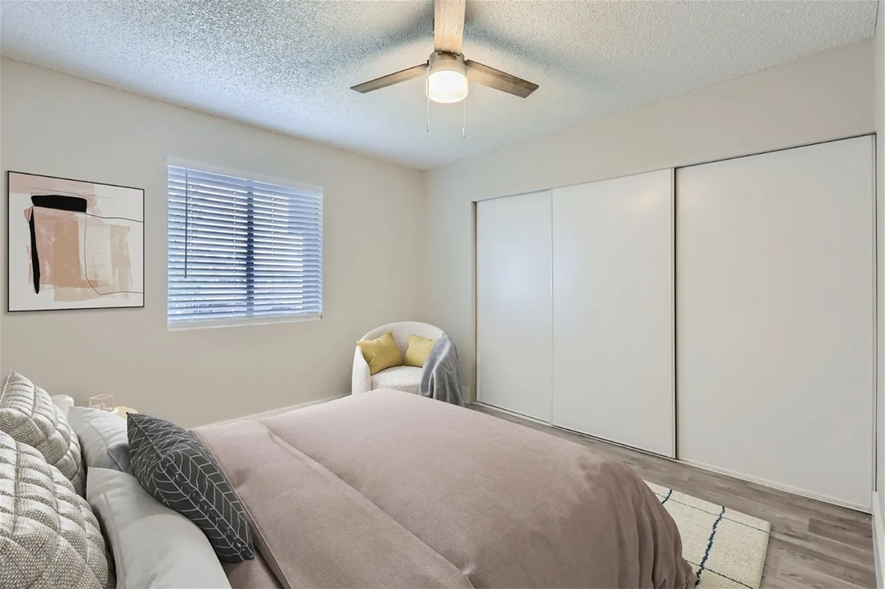 Primary bedroom, bed with pillows, wood-style plank flooring, mirrored closet doors, ceiling fan