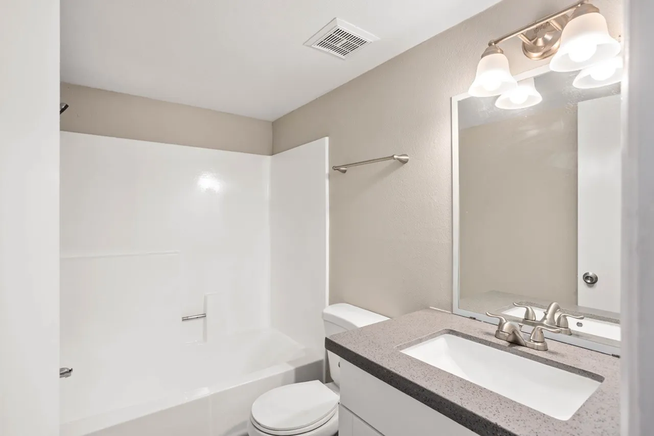 Bathroom, quartz countertop, white single-sink vanity, large mirror with light fixture, white subway tile shower surround