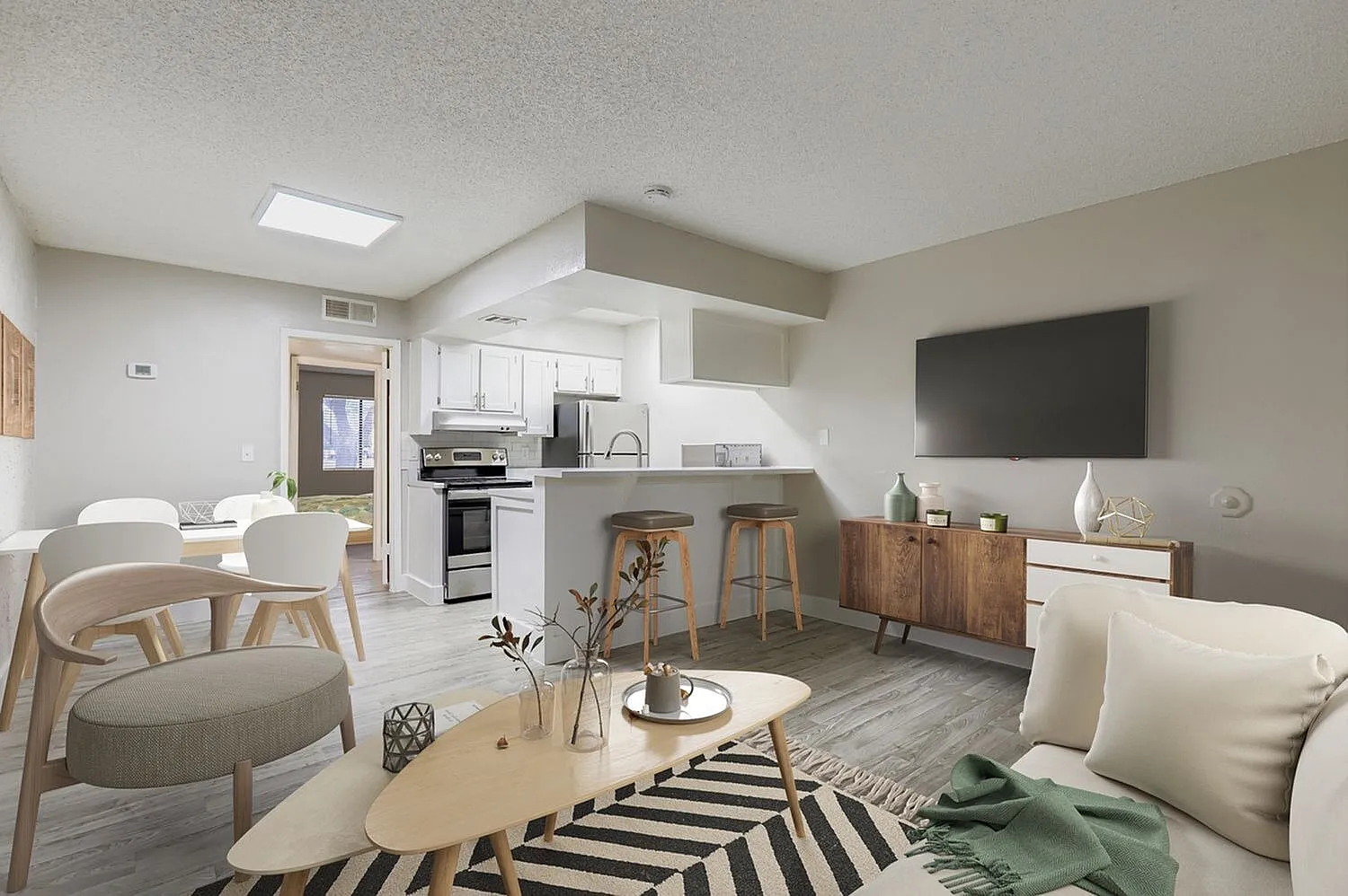 Living room and kitchen area, wood-style plank flooring, white cabinetry, stainless appliances, flat-screen TV
