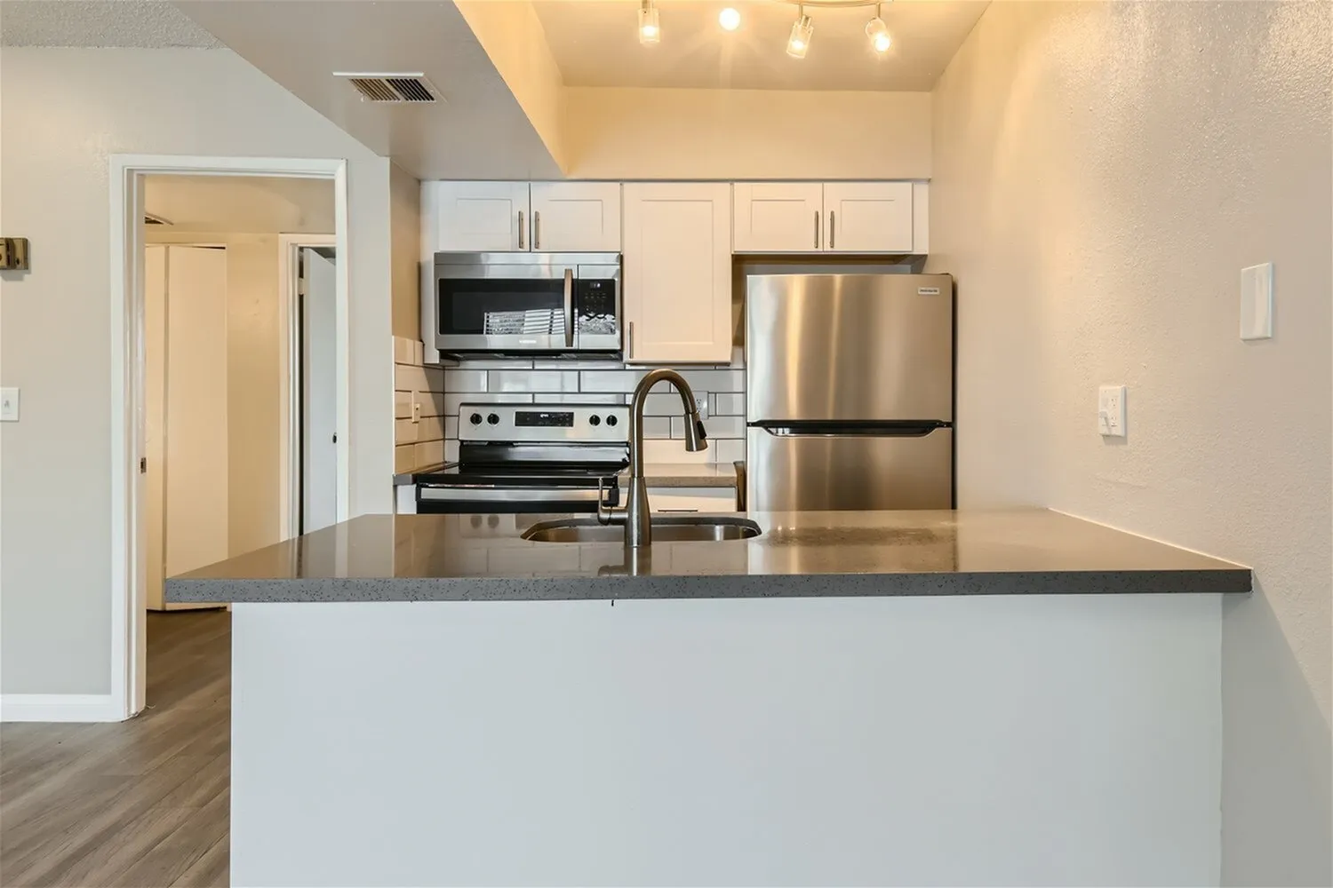 Kitchen, white cabinetry, gray quartz countertops, stainless appliances, wood-style plank flooring