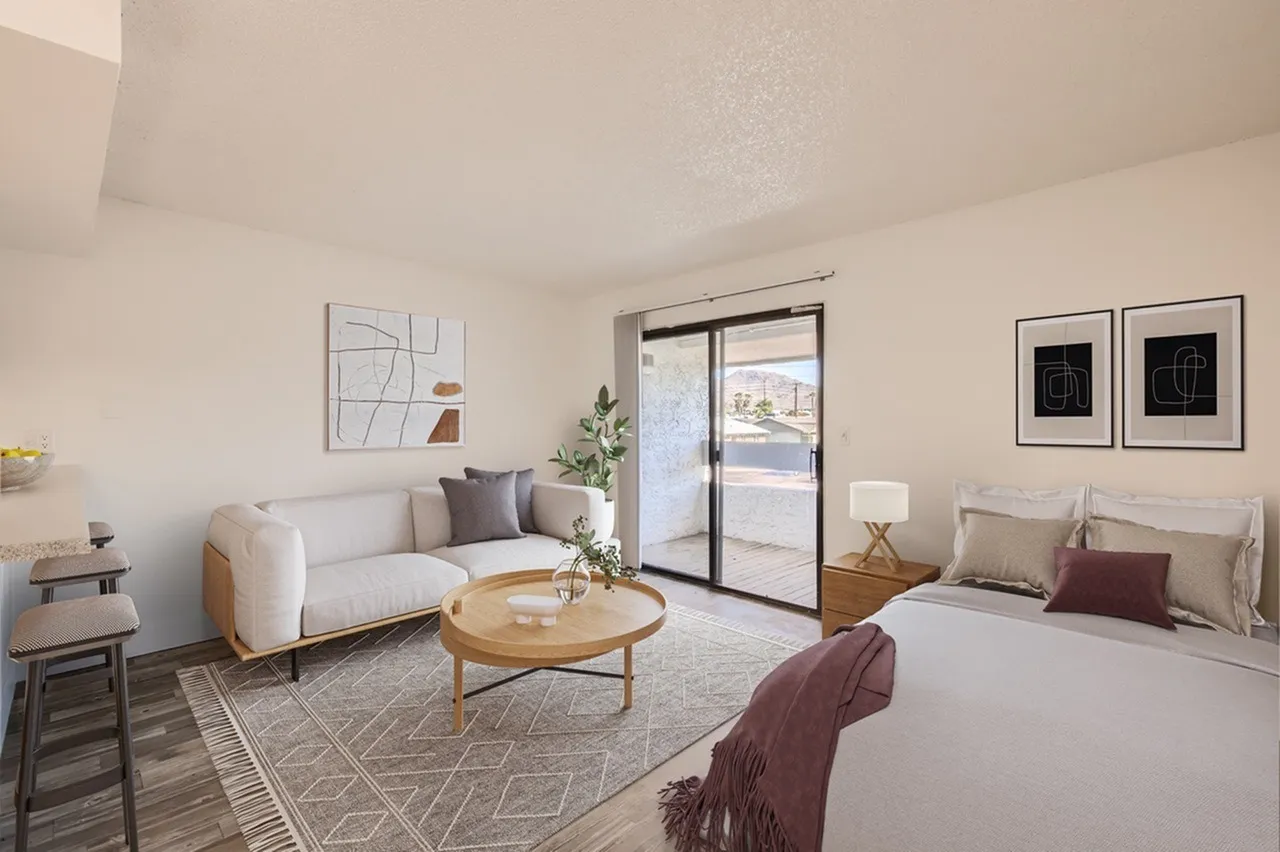 Studio bedroom, cream curved sofa, wood-style plank flooring, sliding glass door, primary bed