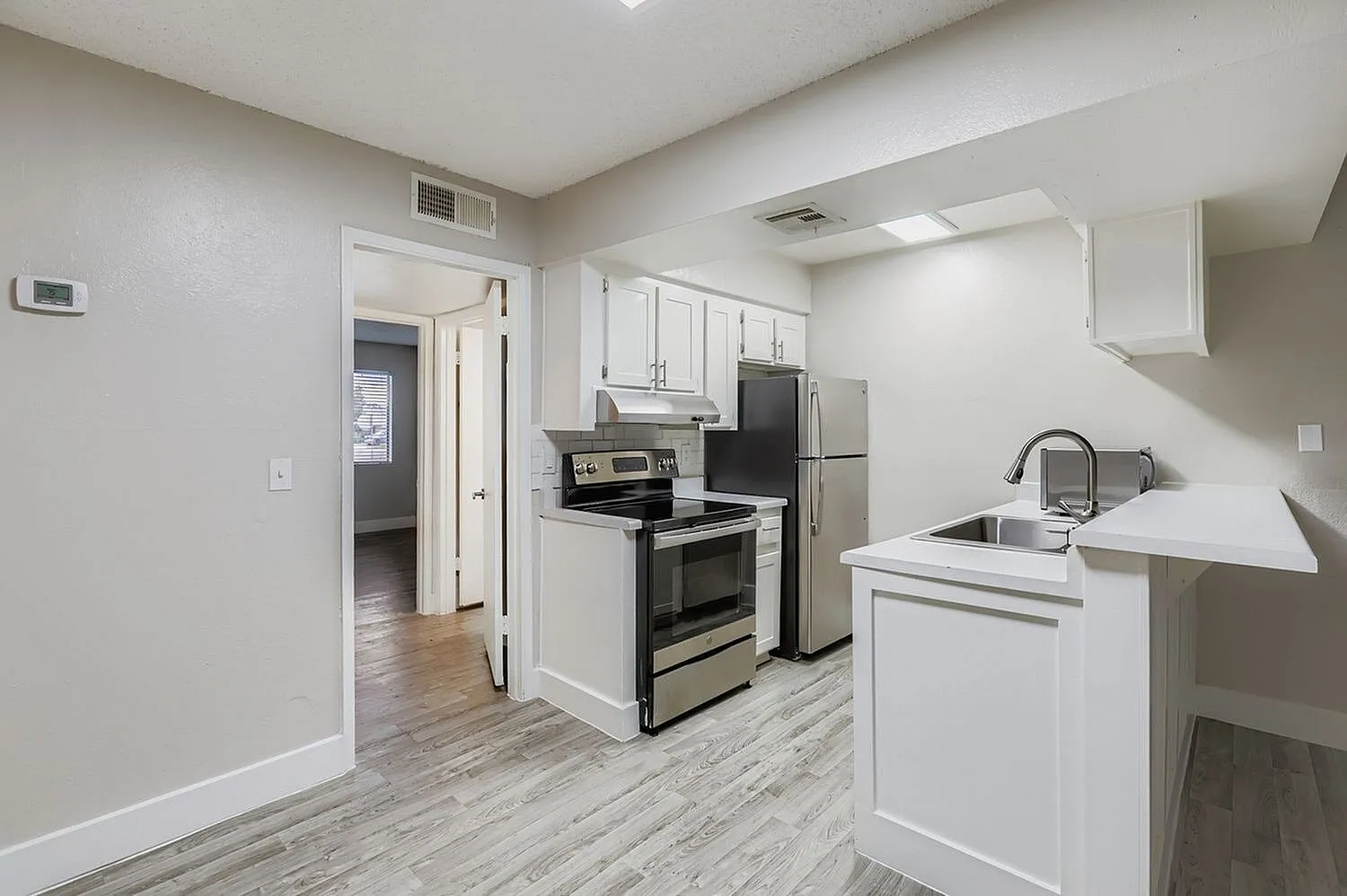 Kitchen, white cabinetry, stainless appliances, wood-style plank flooring, island sink