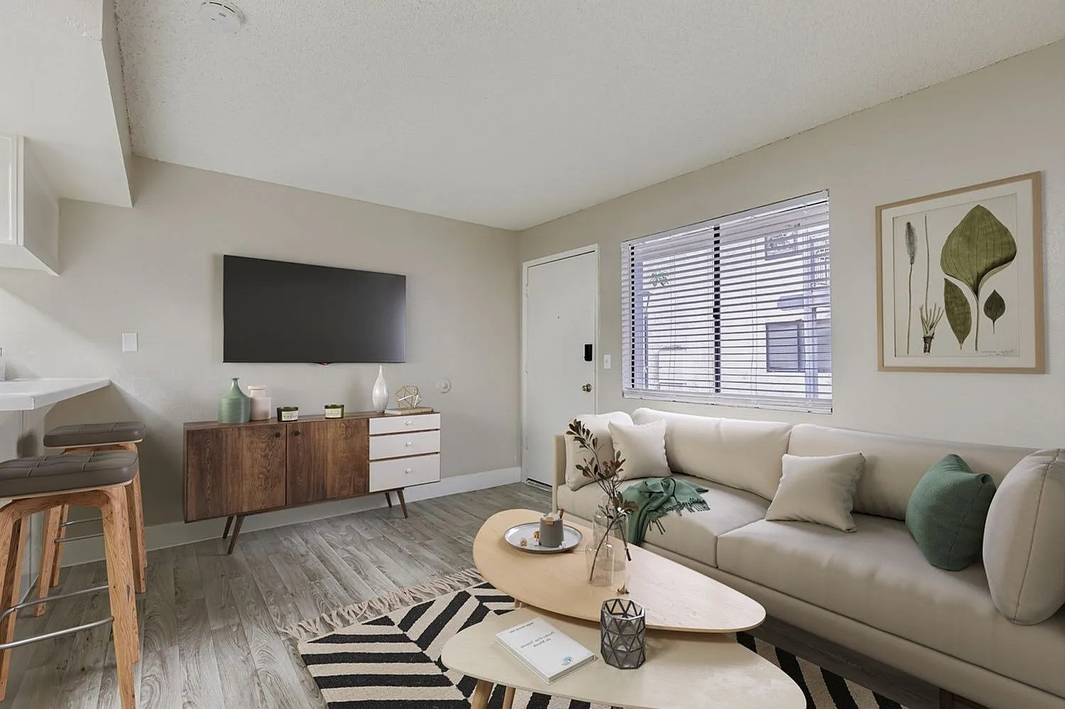 Living room, beige sofa, wood-style plank flooring, mounted TV, green accent pillow