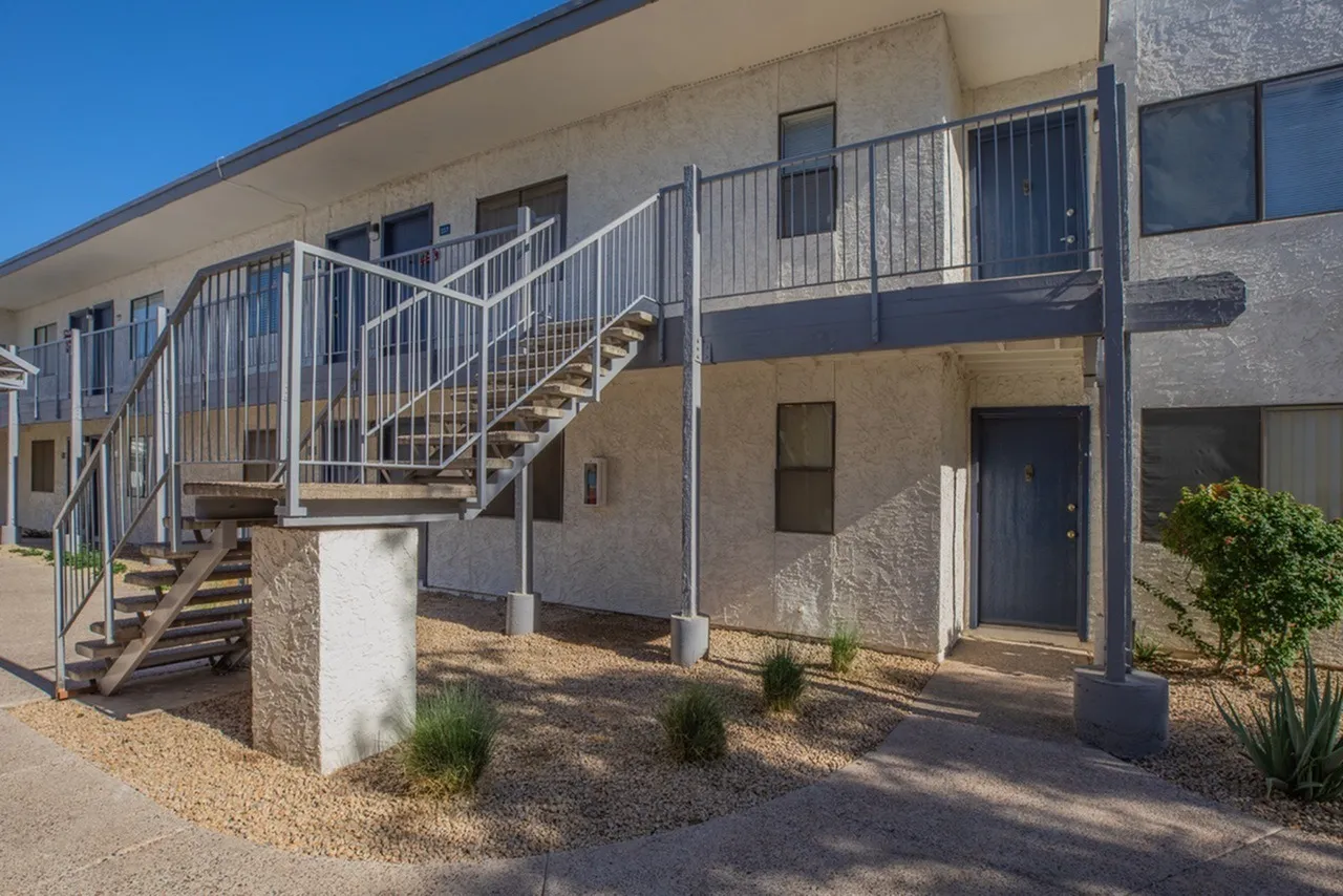 Exterior staircase, metal railings, tan stucco facade, blue doors, landscaping