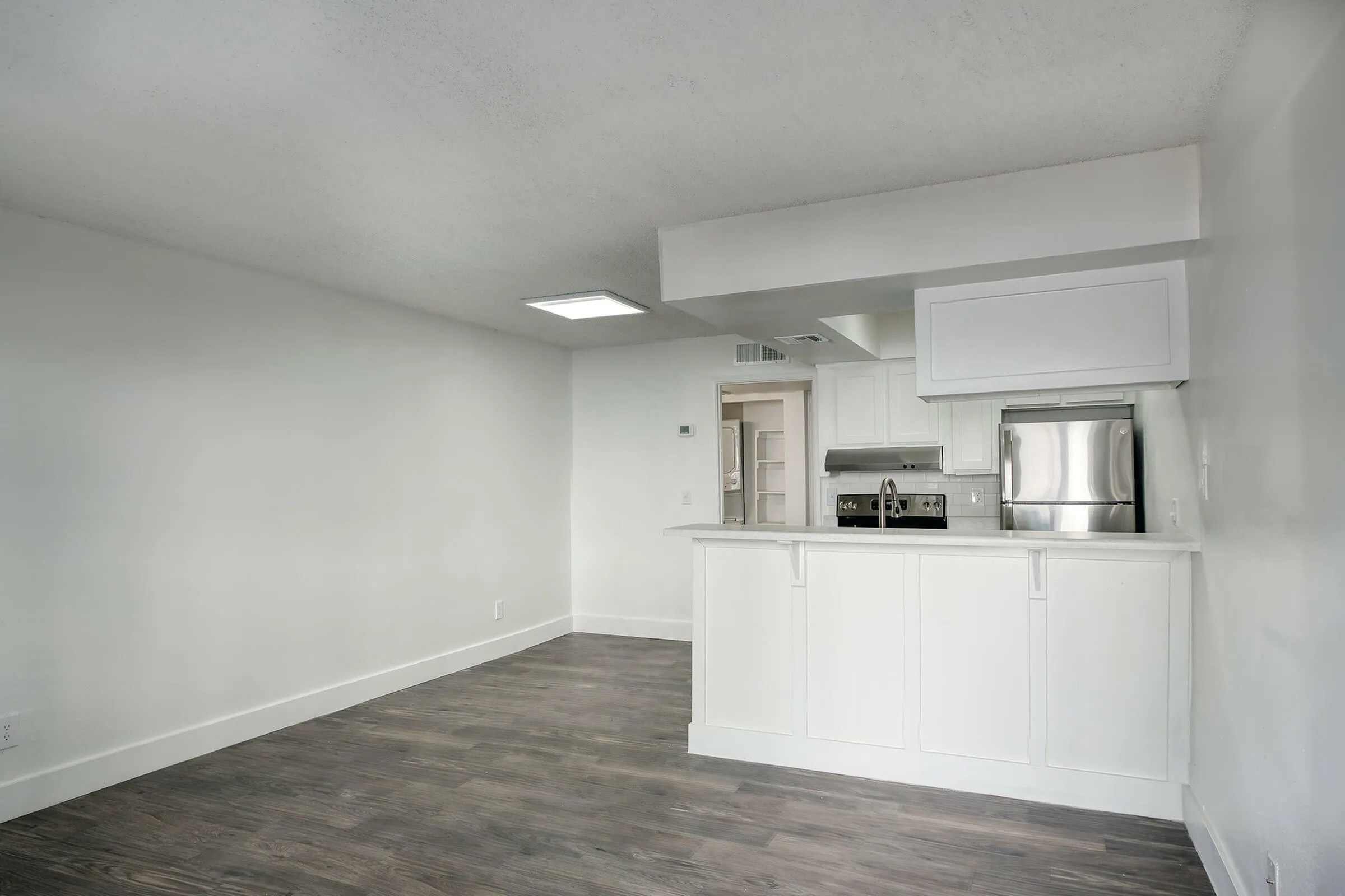 Open concept kitchen and living area, white shaker cabinetry, stainless appliances, wood-style plank flooring