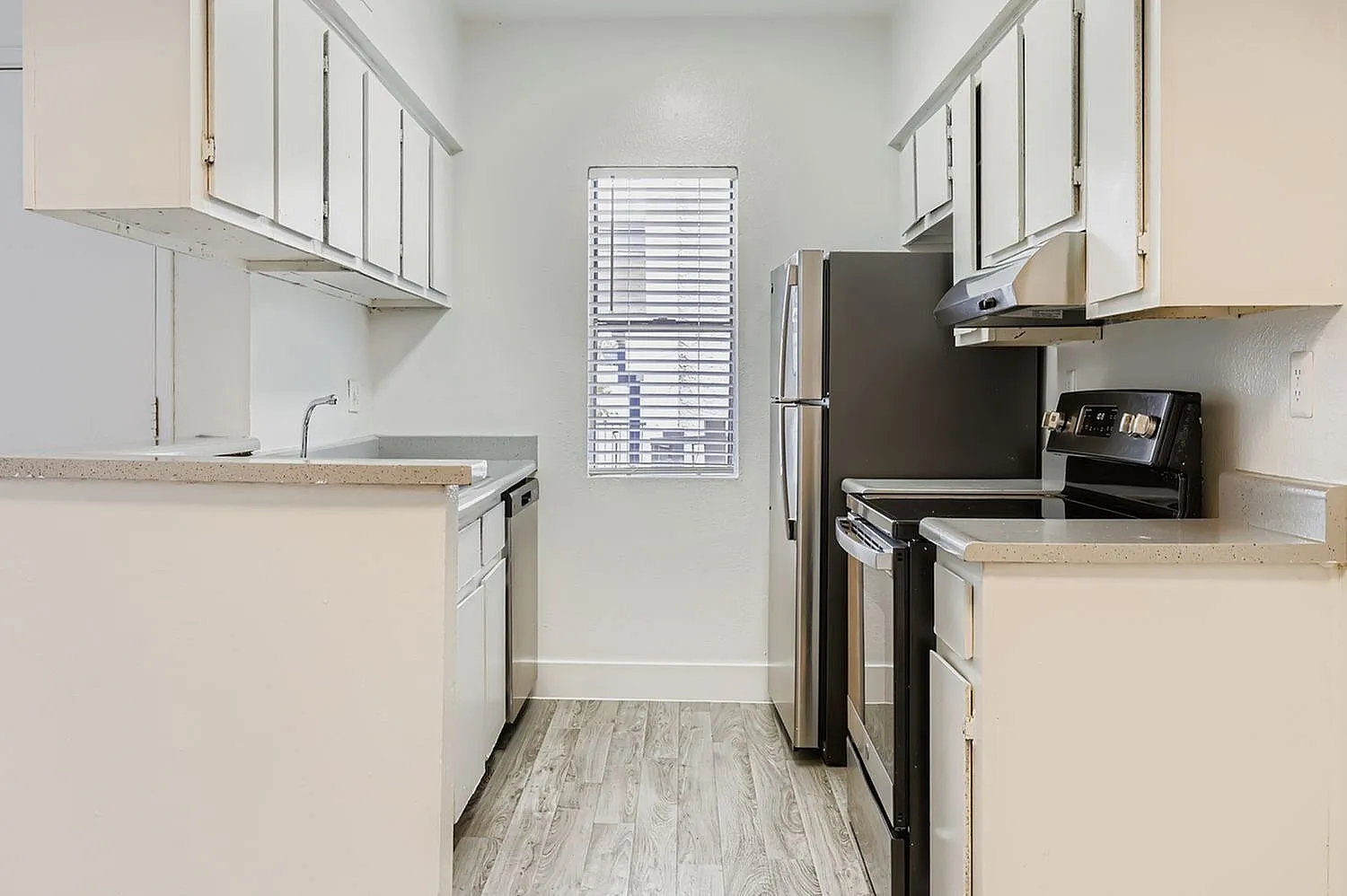Galley kitchen, white shaker cabinetry, light quartz countertops, stainless appliances, wood-style plank flooring