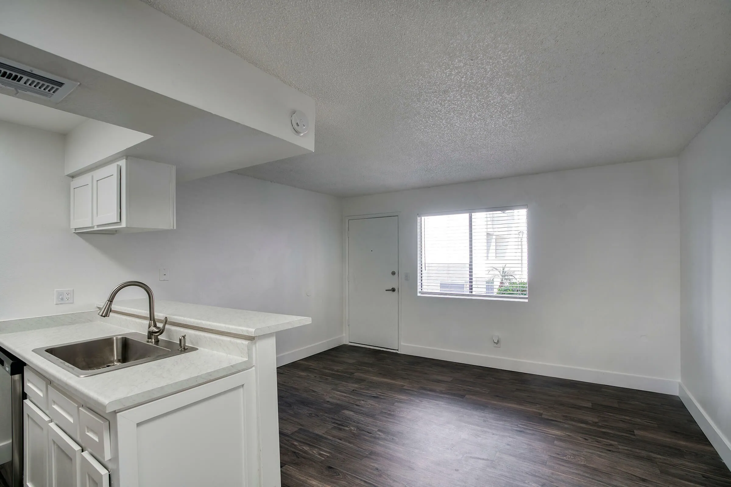 Kitchen with white cabinetry, quartz countertop, sink, adjacent dining space with wood-style plank flooring, window