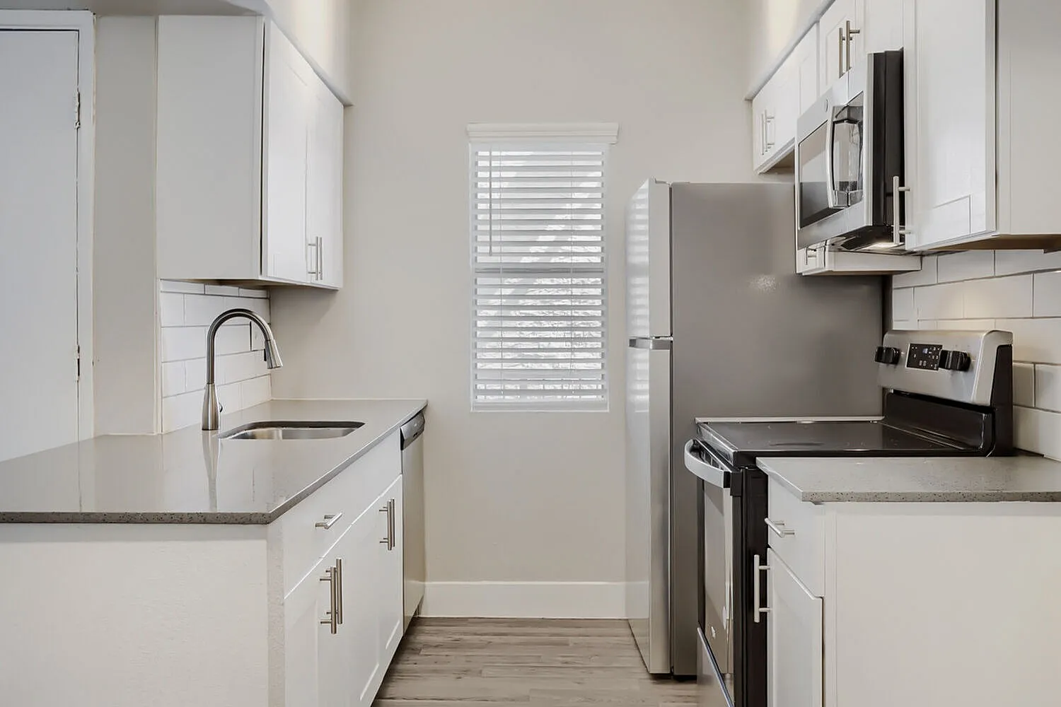Kitchen, white cabinetry, stainless steel appliances, quartz countertops, wood-style plank flooring