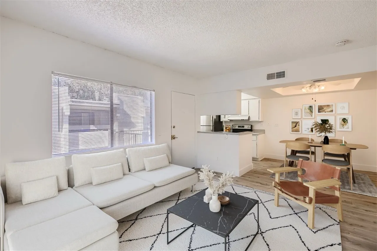 Living room with light gray sectional sofa, black marble coffee table, geometric area rug, wood-style plank flooring, open kitchen with white cabinetry