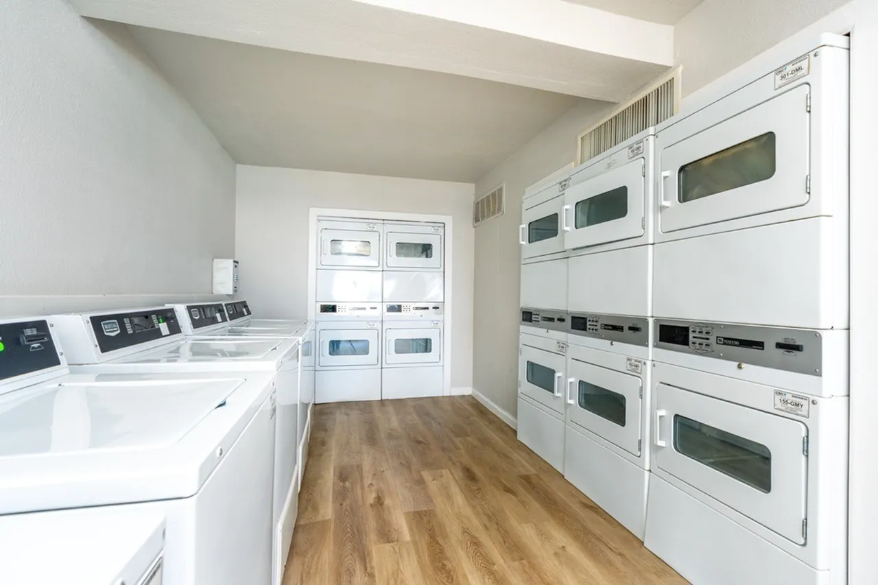 Laundry room, stacked white dryers and washers, wood-style plank flooring, built-in cabinetry