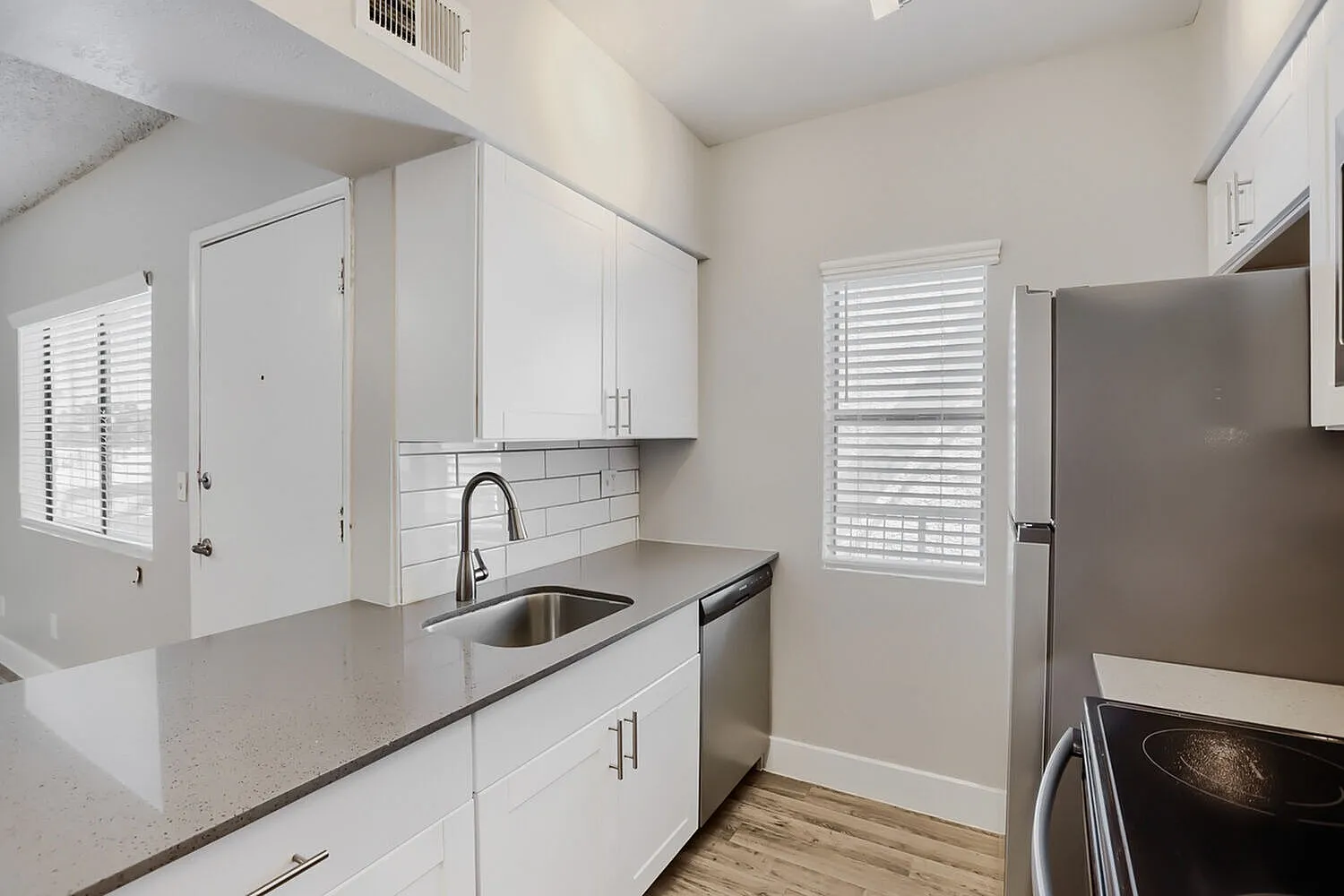 Kitchen, white shaker cabinetry, white subway tile backsplash, stainless sink and faucet, stainless refrigerator, wood-style plank flooring