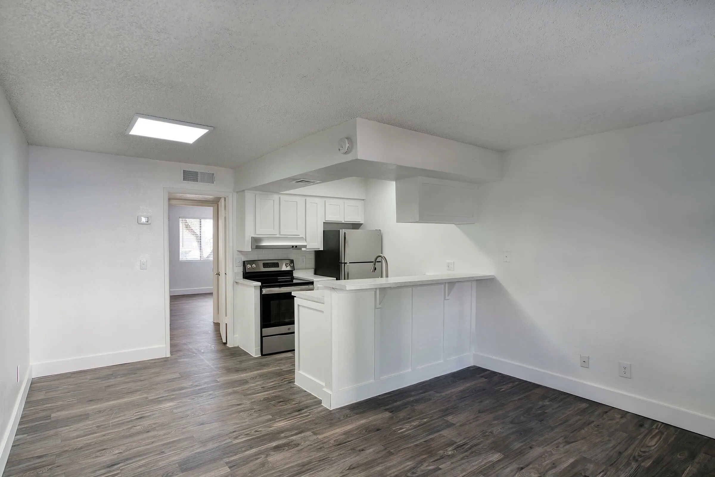 Kitchen and living space, white cabinetry, stainless steel appliances, wood-style plank flooring, island counter