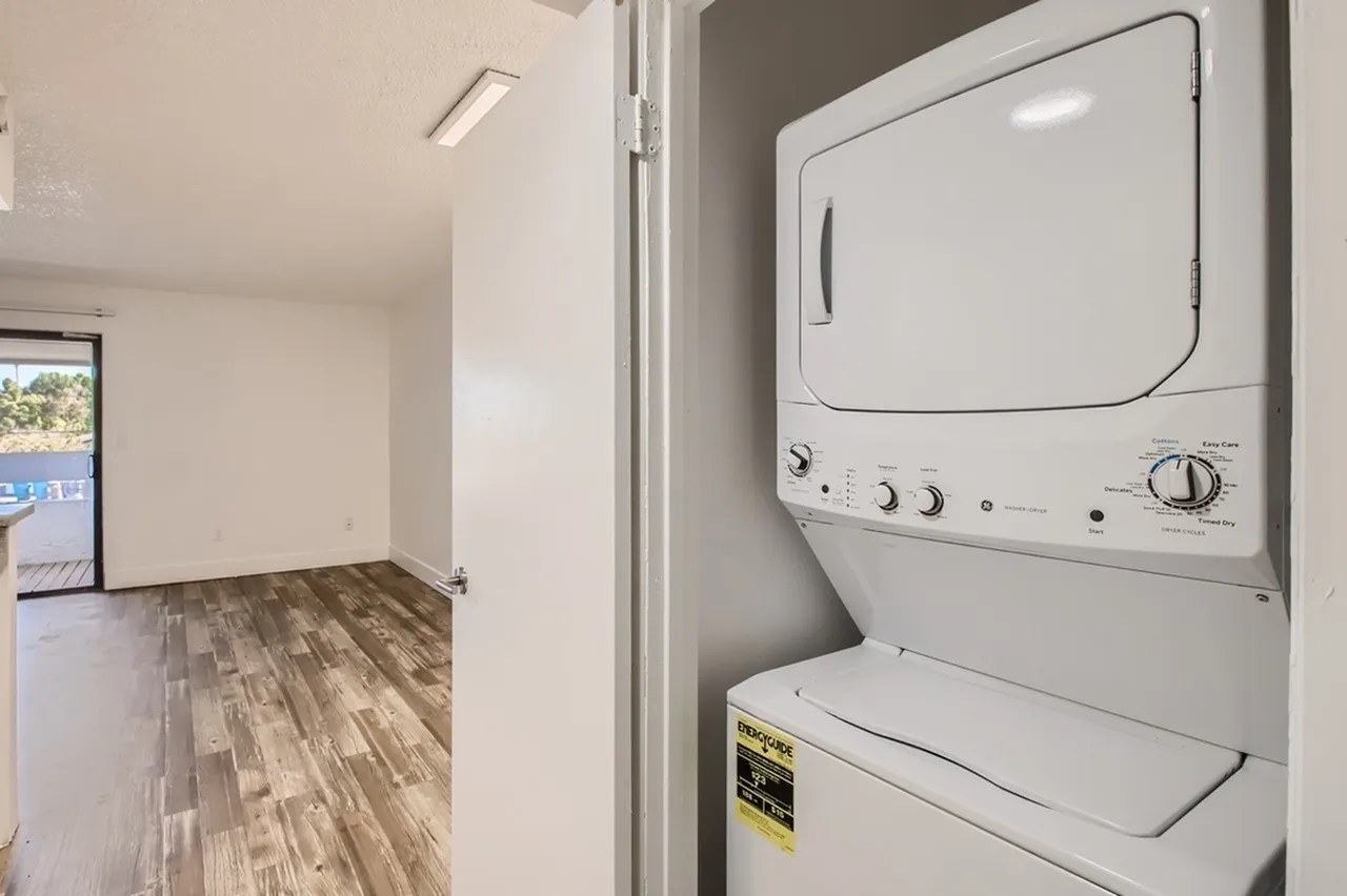 Laundry room, stacked dryer and washer, white appliances, wood-style plank flooring, entryway view
