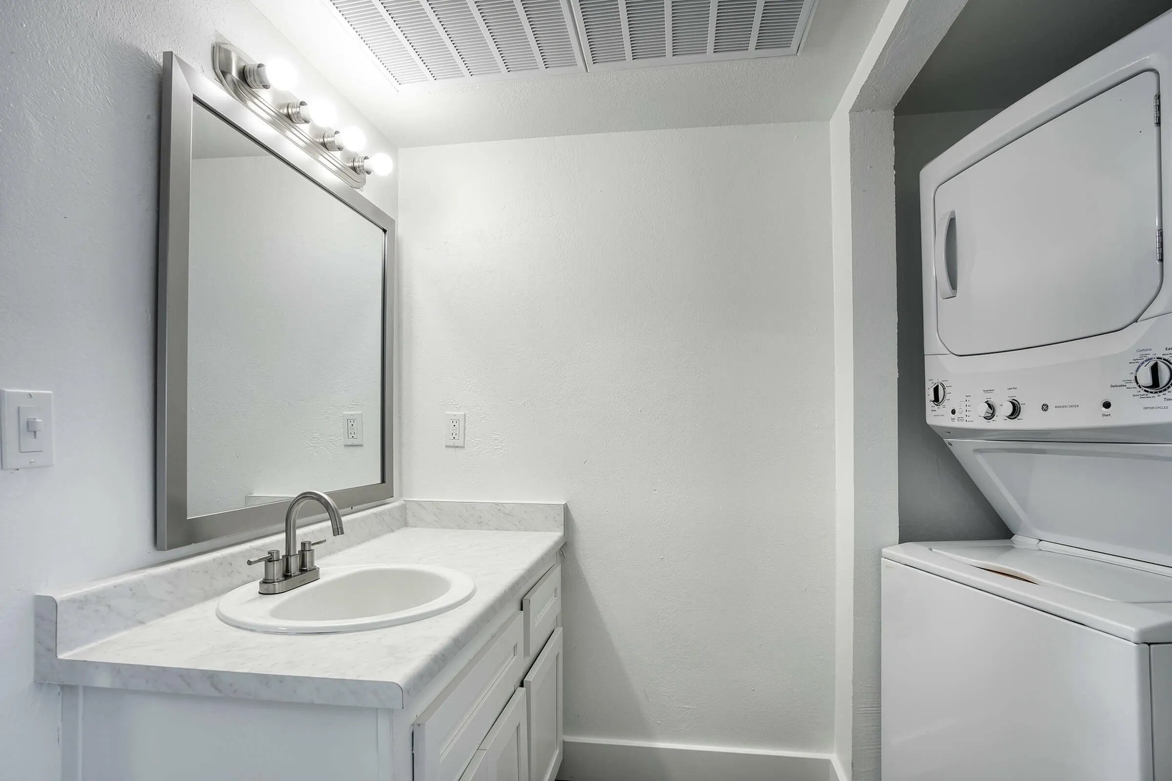 Bathroom, round vessel sink, gray vanity cabinetry, stacked washer dryer, white subway tile