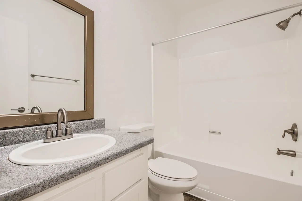 Bathroom, gray speckled countertops, white oval sink, framed mirror, white subway tile shower surround