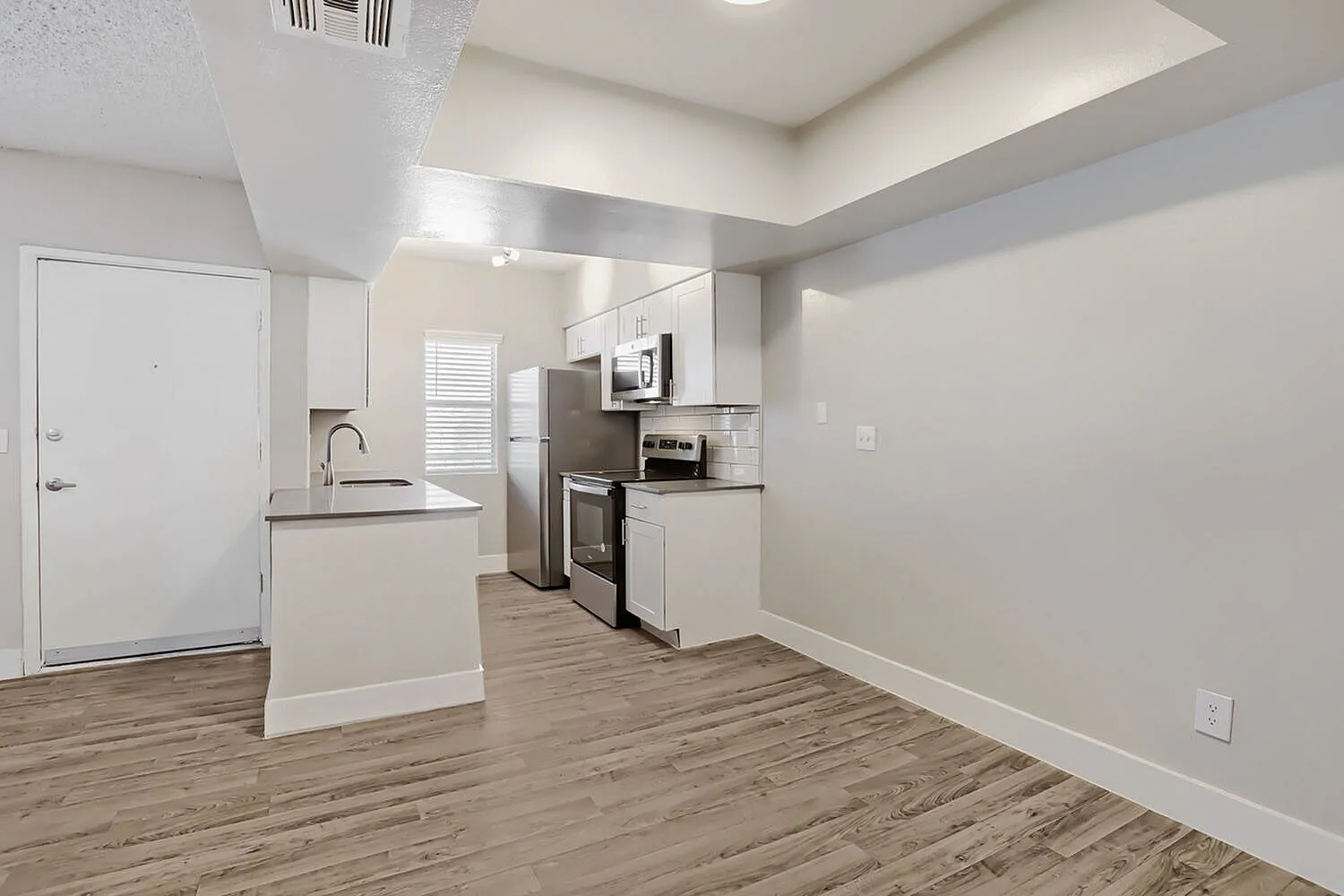 Kitchen with white cabinetry, stainless steel appliances, white countertops, wood-style plank flooring