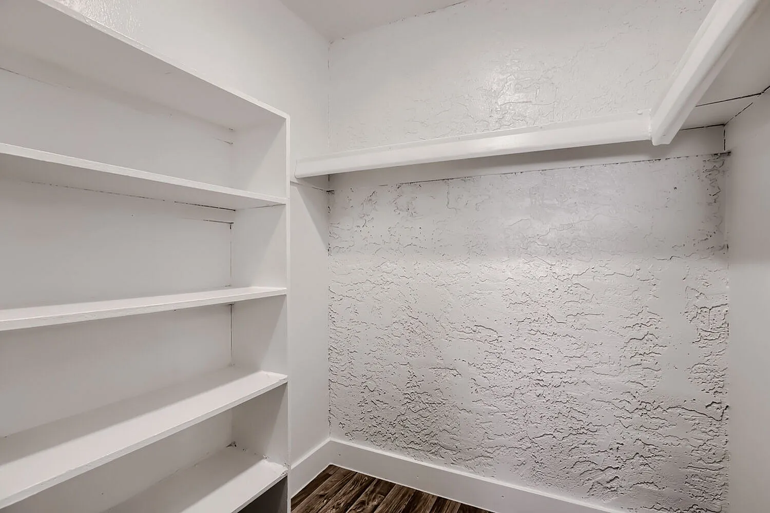 Walk-in closet, white built-in shelves, textured wall, wood-style plank flooring