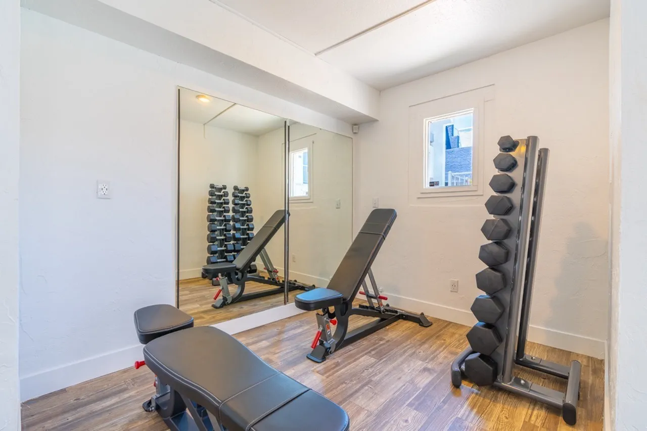 Home gym, mirrored wall, weight dumbbells, adjustable benches, wood-style plank flooring