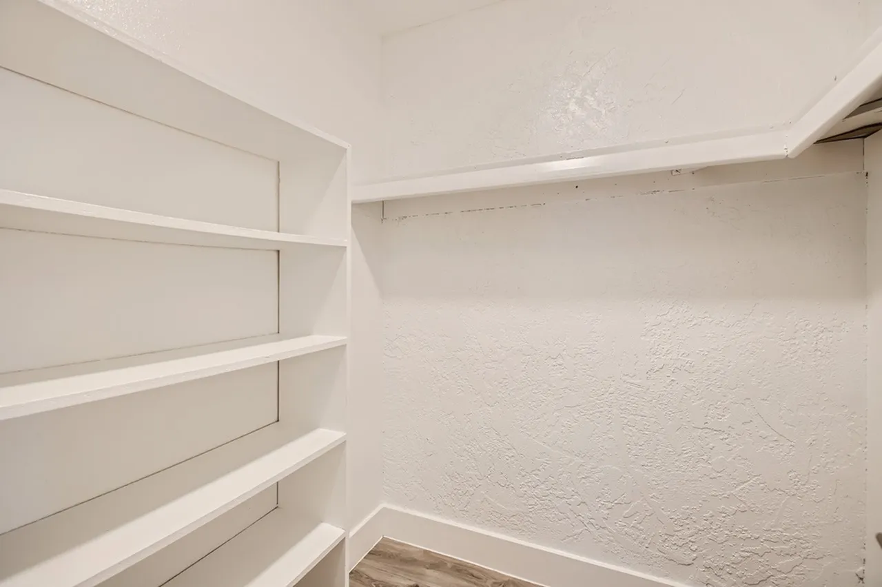 Walk-in closet, white built-in shelving, white walls, recessed ceiling lighting, wood-style plank flooring