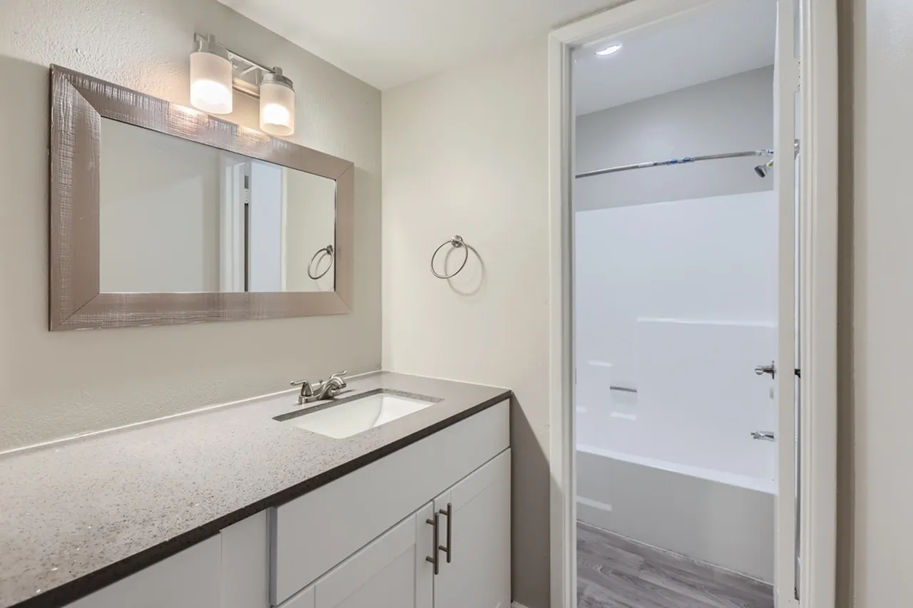 Primary bathroom, gray quartz countertops, white shaker cabinetry, framed mirror, chrome fixtures