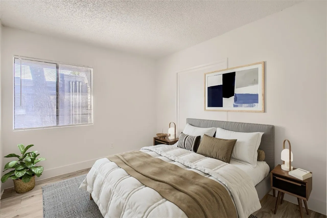 Primary bedroom, gray upholstered headboard, white bedding, wood-style nightstands, abstract framed artwork