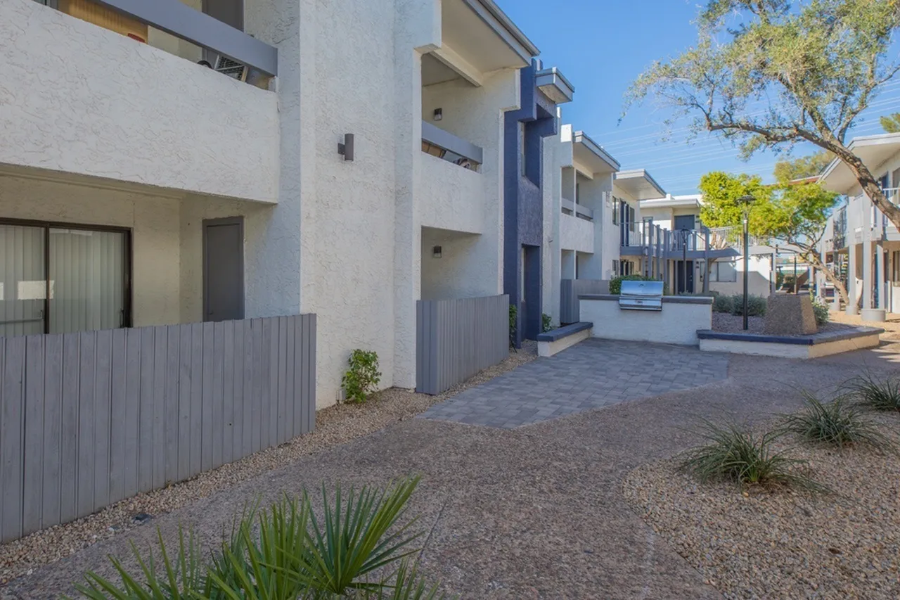 Exterior courtyard, multi-story residential buildings, corrugated metal fencing, paver walkway, desert landscaping