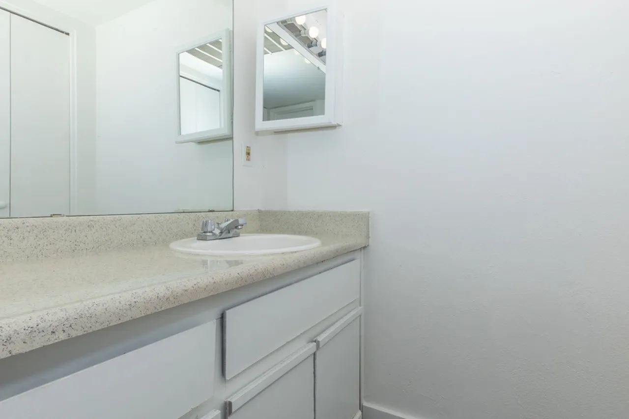 Bathroom, round white sink, speckled light gray countertops, white cabinetry, framed mirror