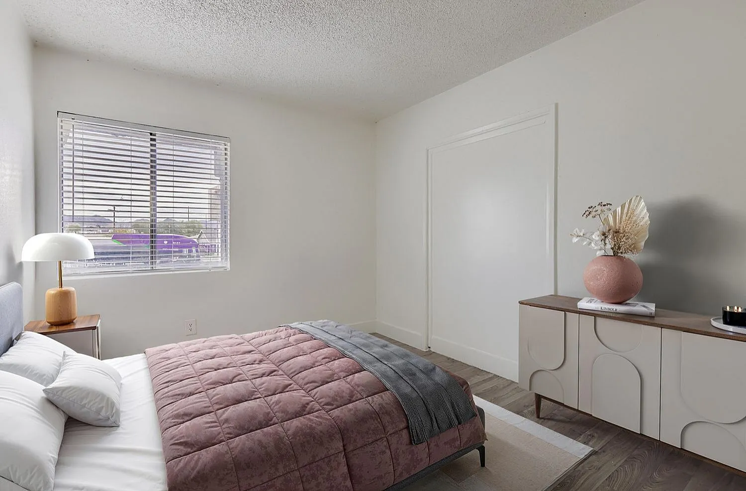 Primary bedroom, mauve quilted comforter, white shutters, wood-style plank flooring