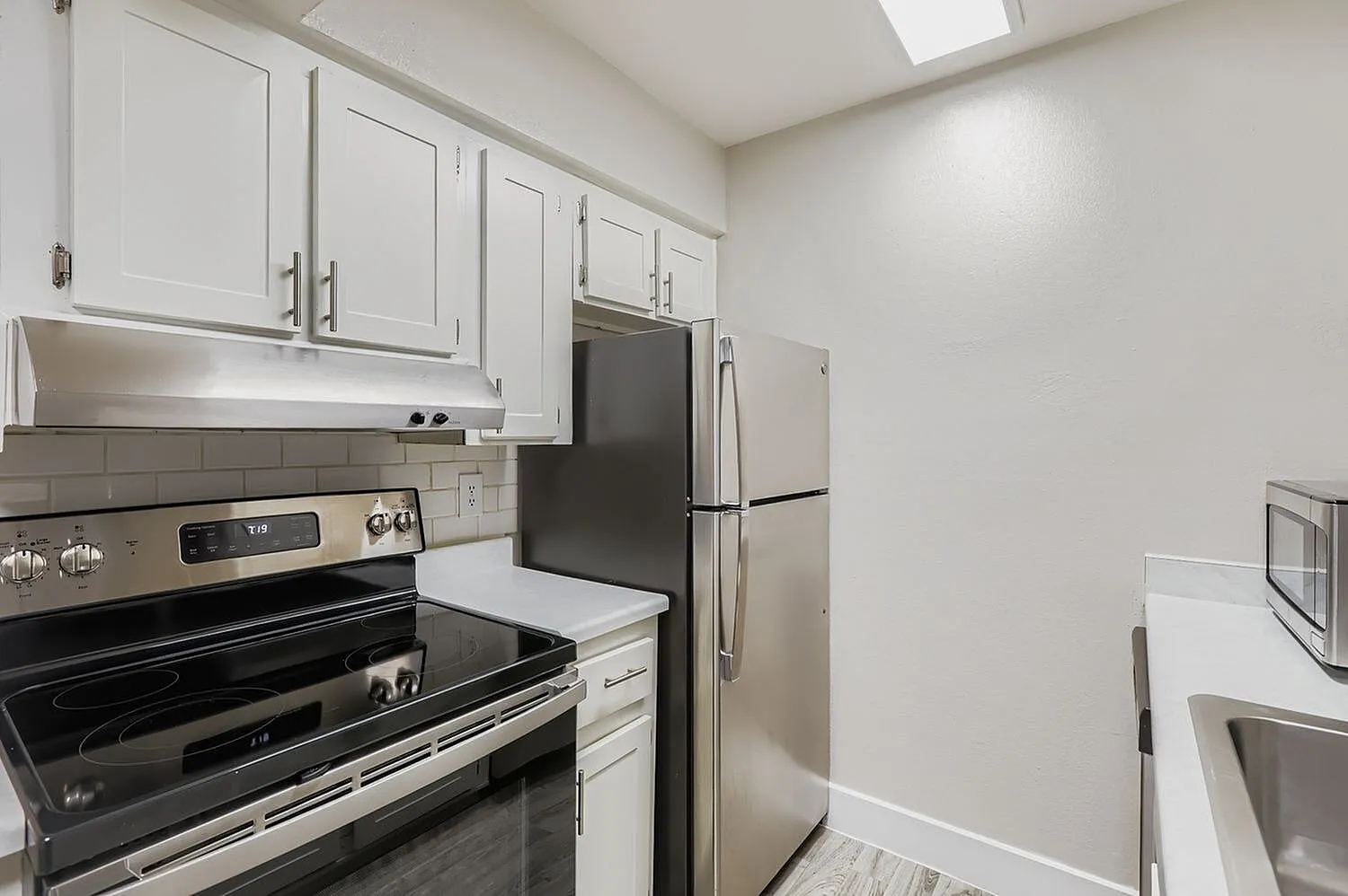 Kitchen, white shaker cabinetry, stainless steel appliances, gray tile backsplash, wood-style plank flooring