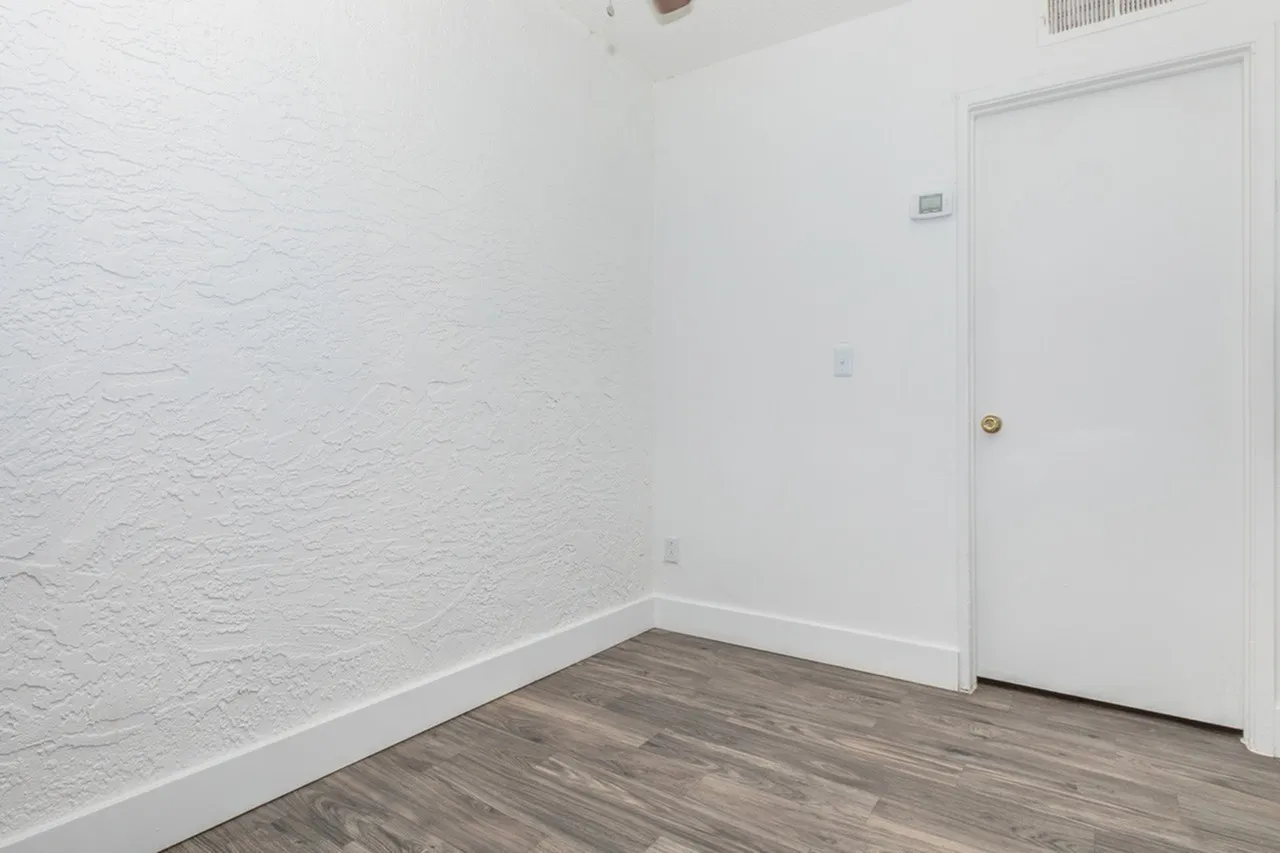 Bedroom, white textured walls, wood-style plank flooring, white door with brass knob