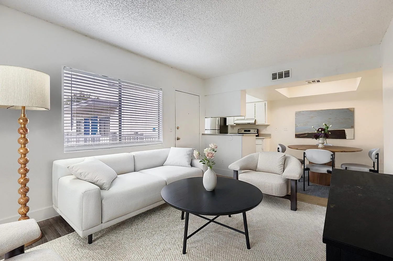Living room with white sectional sofa, black round coffee table, wood-style plank flooring, open kitchen with white cabinetry