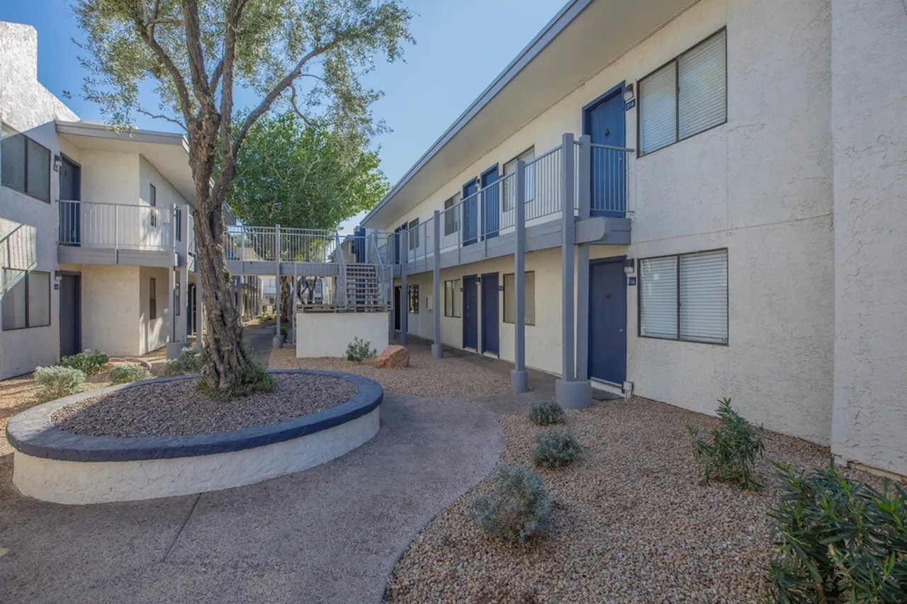 Courtyard with mature tree, circular planter, gravel landscaping, blue railings, two-story building