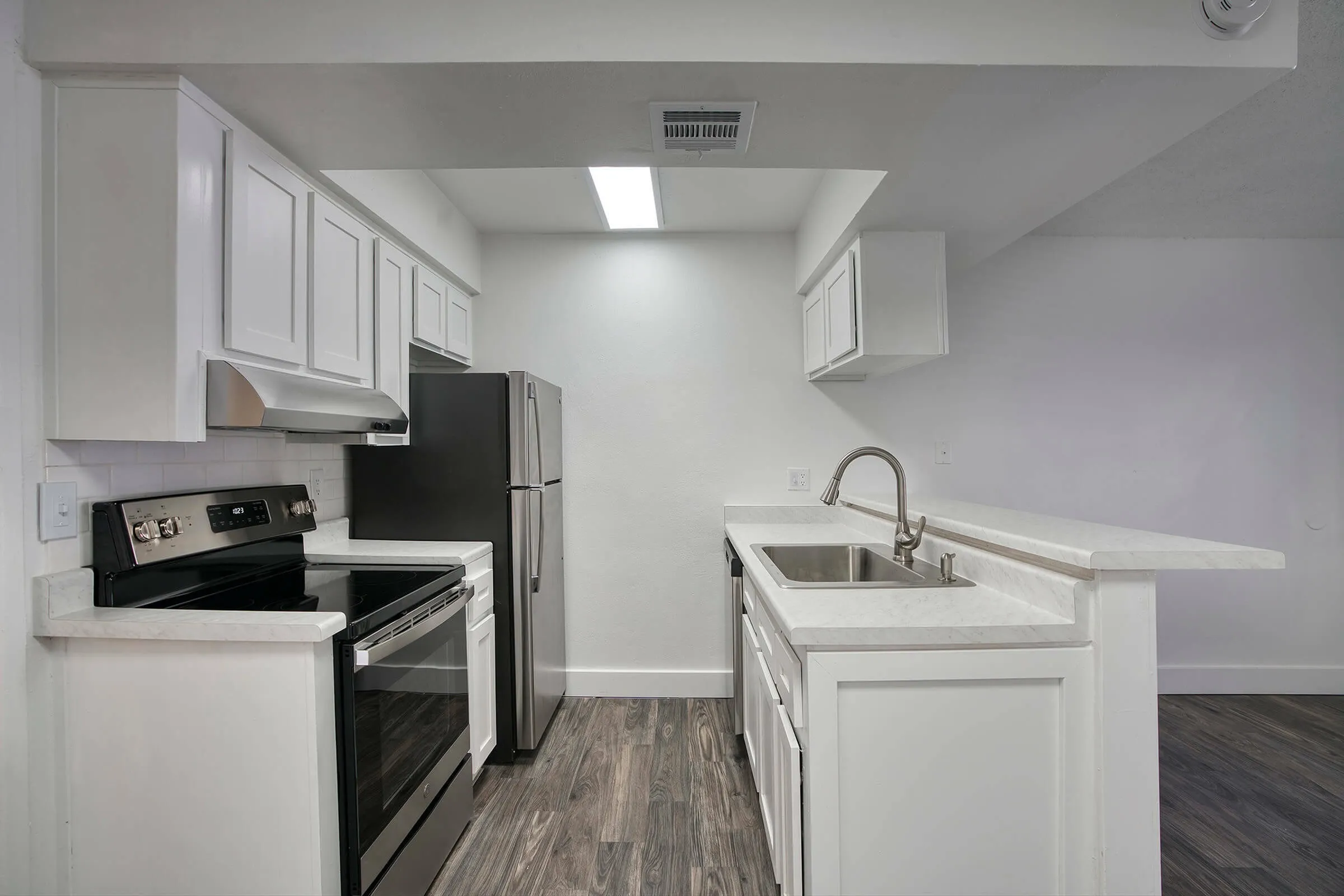 Kitchen, white shaker cabinetry, stainless appliances, island with sink, wood-style plank flooring