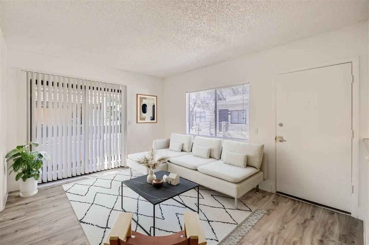 Living room, cream L-shaped sofa, wood-style plank flooring, geometric area rug, black coffee table