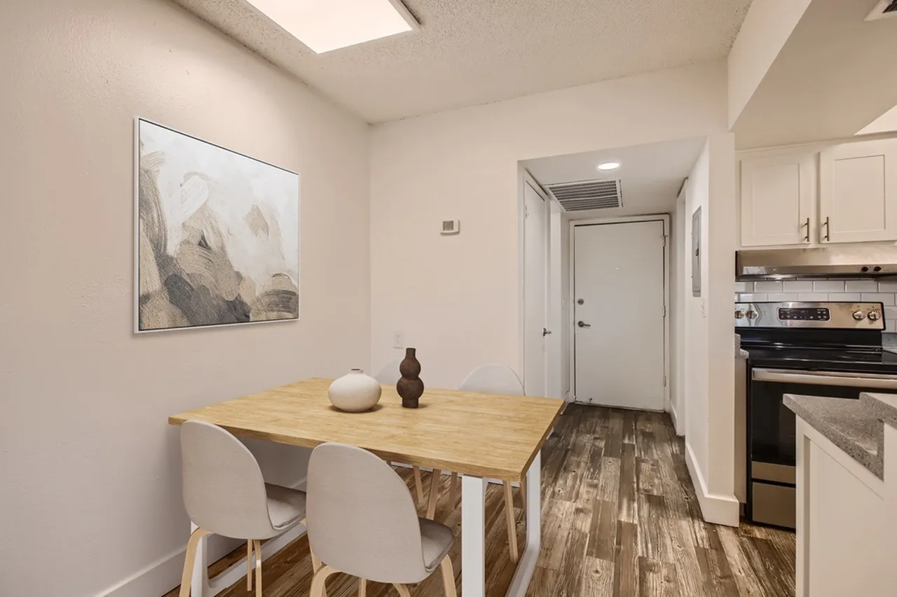 Dining area with wood dining table, white chairs, wood-style plank flooring, stainless steel appliances