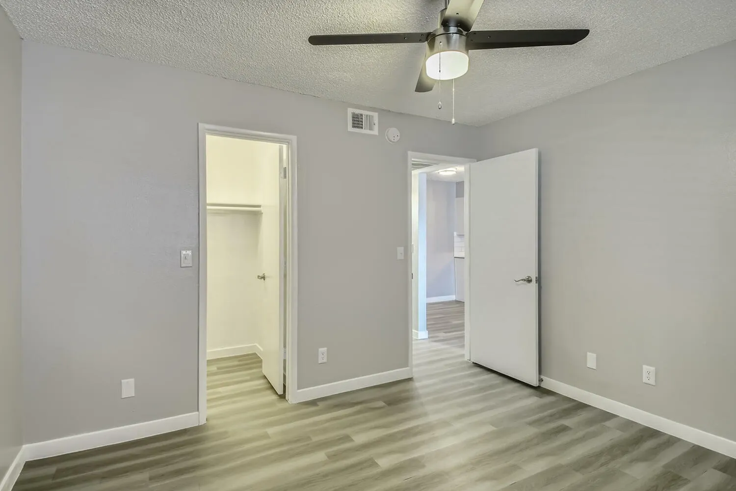Bedroom, wood-style plank flooring, ceiling fan, two entry doors, gray walls